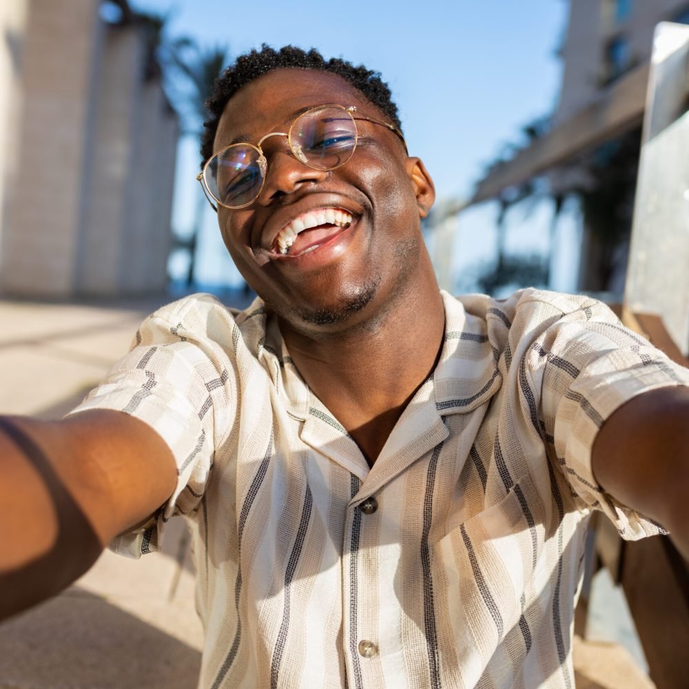 Happy young black man with glasses taking selfie looking at camera. Vertical image. Lifestyle concept.