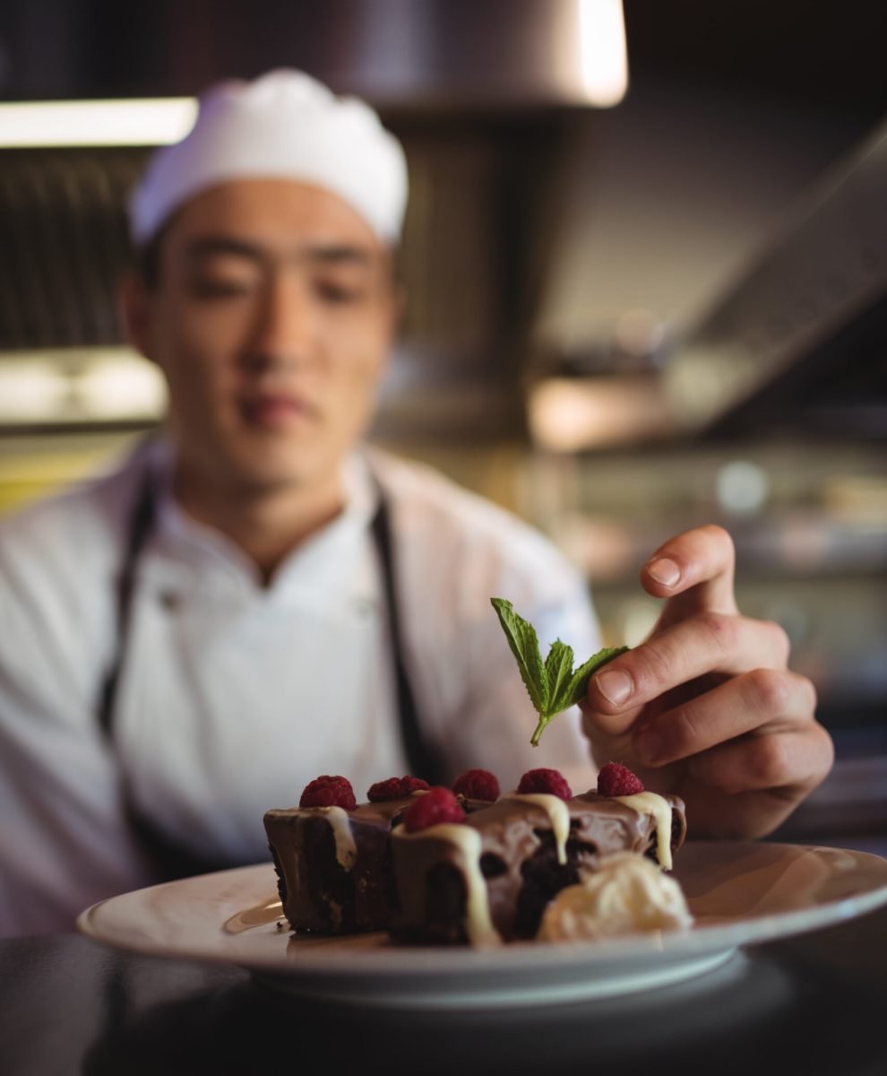 Close-up of male chef garnishing dessert plate in commercial kitchen